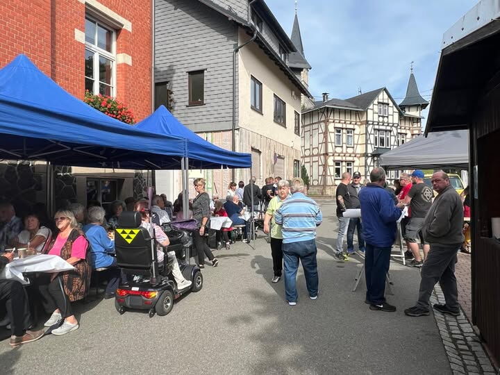Straße mit Menschen, die an überdachten Sitzgruppen sitzen und feiern